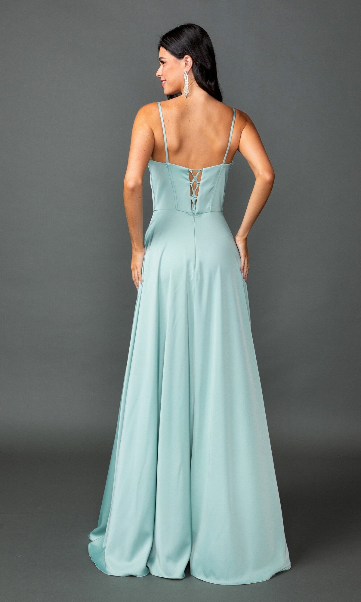 A woman stands against a gray background, facing away from the camera, wearing the Dancing Queen 4544 long prom dress in light teal with spaghetti straps and a lace-up back.